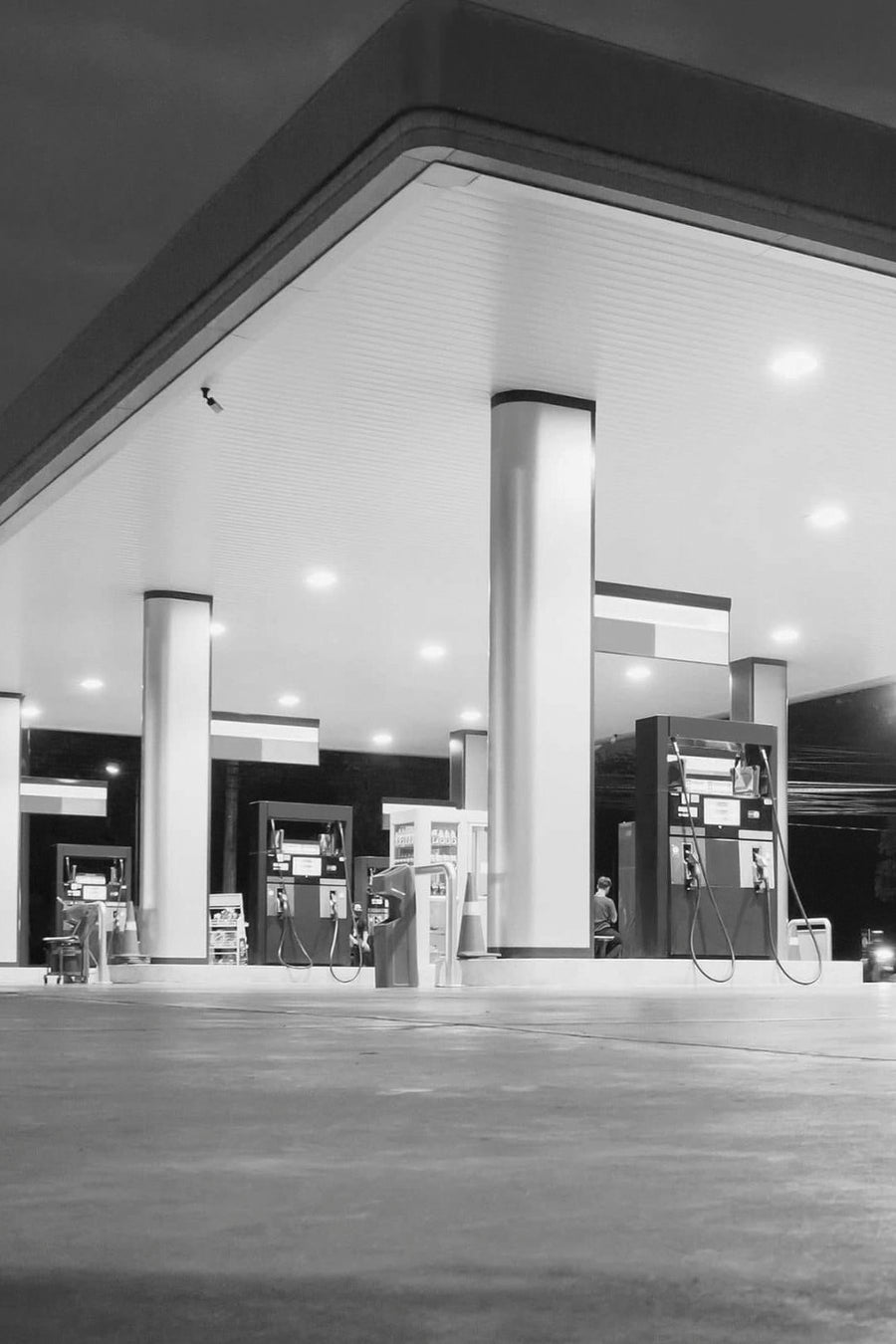 Black and white photograph of a brightly lit petrol station under a large canopy at night.